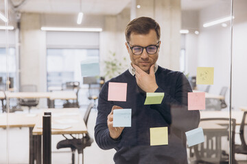 Businessman analyzing ideas on colorful sticky notes in a modern office setting, reflecting on strategic planning and innovation