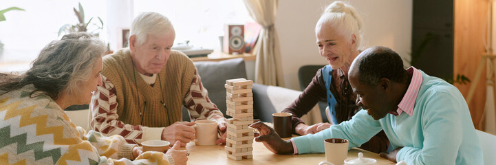 Website banner with biracial pensioners playing board game together, they trying to construct high...