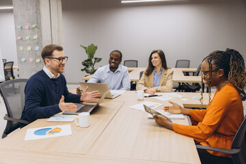 Diverse professionals collaborating, reviewing data charts and digital devices during strategic planning session in modern workplace setting