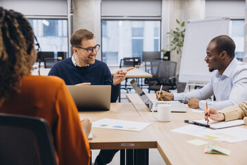 Diverse professionals collaborating, analyzing charts on laptops, working together in modern office environment with shared focus