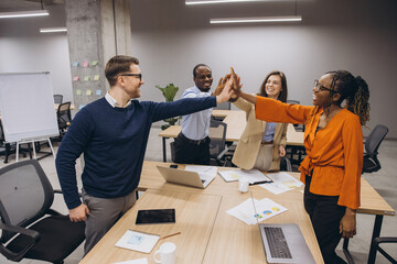 Diverse businesspeople high fiving, celebrating collaborative achievement with enthusiasm in...