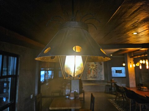 Close-up of a rustic hanging lamp with a metal shade, creating a warm ambiance in a dimly lit café