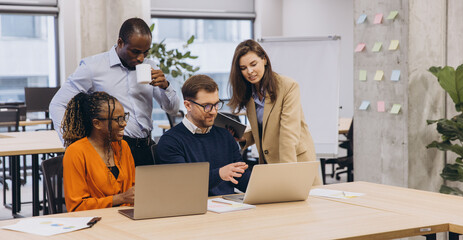 Professional team engaging in collaborative work around laptops, discussing projects in a...