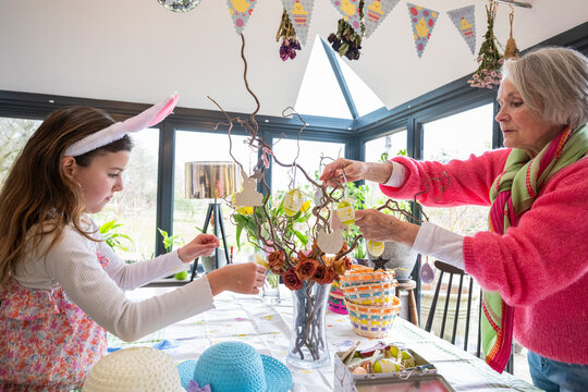 Grandmother and grandchild arranging Easter ornaments on kitchen table.