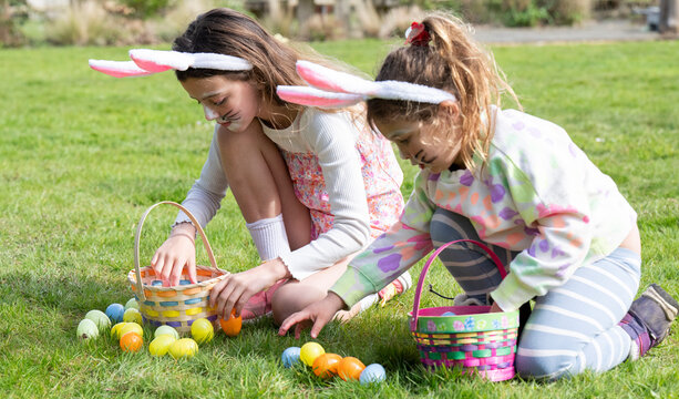 Two girls collecting Easter eggs in gardenwearing bunny ears