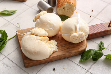 Wooden board of tasty Burrata cheese with basil on white tile background