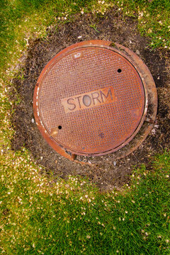A rusting storm sewer manhole cover on a storm sewer drain.