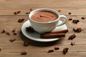 Cup of tasty melted chocolate with cinnamon sticks and star anise on wooden background