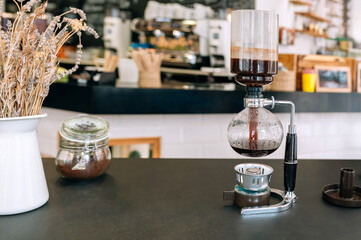 Japanese siphon coffee maker brewing fresh coffee on a countertop in a empty modern cafe seating. Traditional brewing method highlight the art of coffee preparation. Copy space available in image.