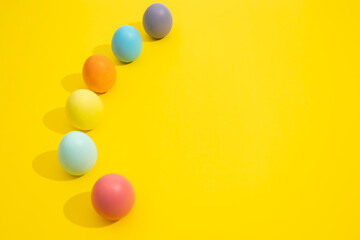 Easter eggs of various colors lined up on a yellow background with copy space. Easter decoration