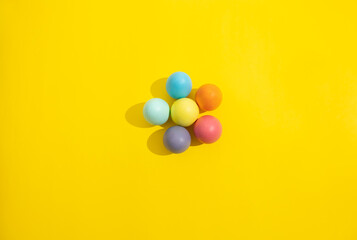 Easter eggs of various colors making the shape of a flower on a yellow background. Easter decoration concept