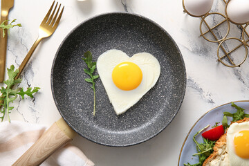 Frying pan with tasty fried egg in shape of heart on light background