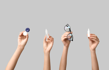 Female hands with eye drops, container with contact lenses and eyeglasses on grey background....