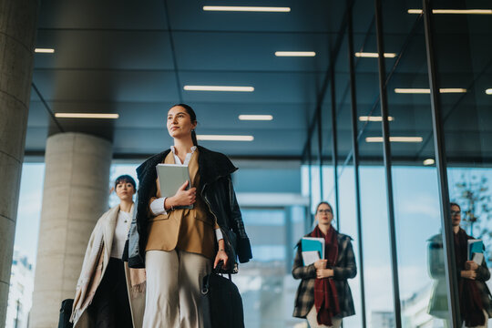 A group of professional women walking confidently through a modern urban area, holding documents and symbolizing collaboration, success, and professionalism in a business-oriented outdoor setting.