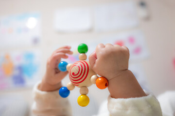 An infant baby hands holding and  playing with a wooden teether toy