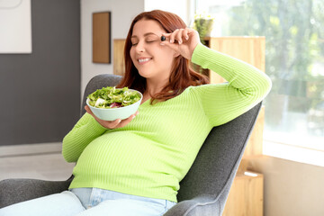 Young pregnant woman with fresh vegetable salad sitting on armchair at home