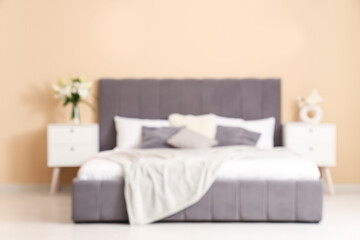 Interior of bedroom with vases of lily flowers on bedside tables near comfortable bed, blurred view