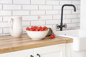 Bowl and basket with tasty strawberries near sink in kitchen