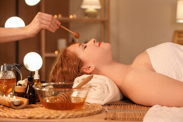 Massage therapist pouring honey on woman's face in dark spa salon, closeup