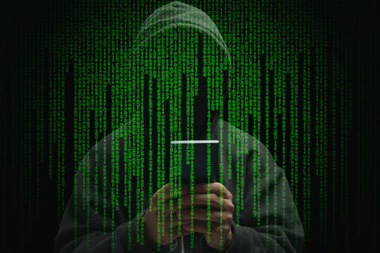 Hacker in hood holding a cellphone on matrix code background. Scam cyber crime concept
