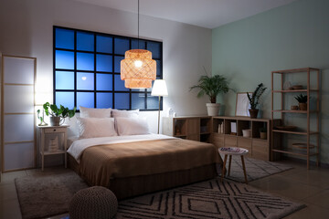 Interior of bedroom with comfortable bed, bedside table and glowing lamps