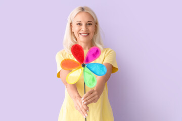 Mature woman with toy windmill on lilac background