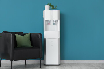 Modern water cooler and armchair near blue wall in office