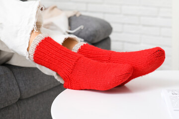 Woman in red knitted socks sitting on sofa at home, closeup