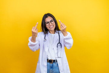 Young brunette doctor woman wearing stethoscope standing over isolated yellow background showing middle finger doing fuck you bad expression, provocation and rude attitude. screaming excited