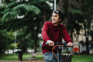 Obraz premium Young man in a red sweater riding an electric scooter in a park, smiling, and enjoying the outdoor environment. Green trees in the background create a calm and pleasant atmosphere.