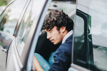 A focused young man exits a car as his parent drops him off for school. The image captures a daily...