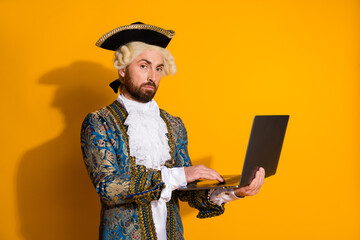 Portrait of an aristocratic nobleman in vintage attire using a modern laptop against a vibrant yellow background