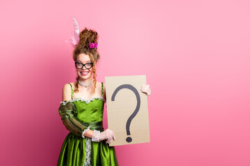 Elegant young woman in a vibrant green gown holding a question mark sign, blending modern and historical themes against a pink background