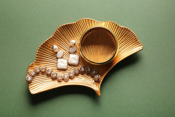 Golden tray with beautiful bracelets and earrings on green background