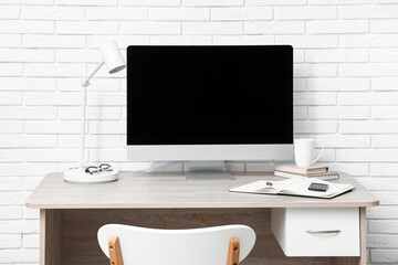 Modern home office with computer near white brick wall in room
