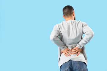 Young man suffering from back pain on blue background