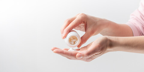 A woman's hand pours white pills from a bottle on a white background. Healthcare concept, nutritional supplements, treatment of depression and disease. Banner