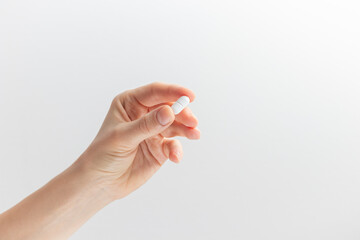 Female hand holding white pill with fingers on white background. Concept of health care, dietary...