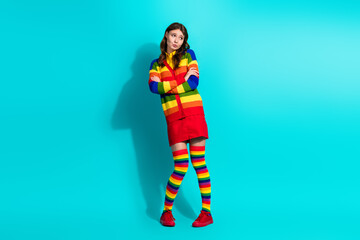 Stylish young woman in vibrant rainbow outfit against turquoise background, expressing...
