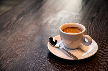 A steaming cup of coffee rests on a small white plate, accompanied by a silver spoon, evoking warmth and tranquility in a stylish cafe setting, perfect for reflection.