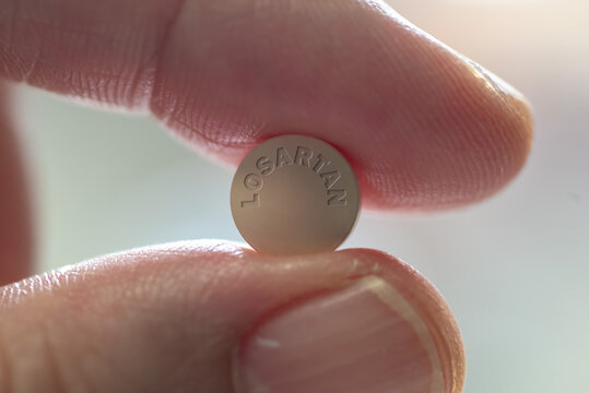 Fingers holding losartan drug tablet high blood pressure medicine - close-up	