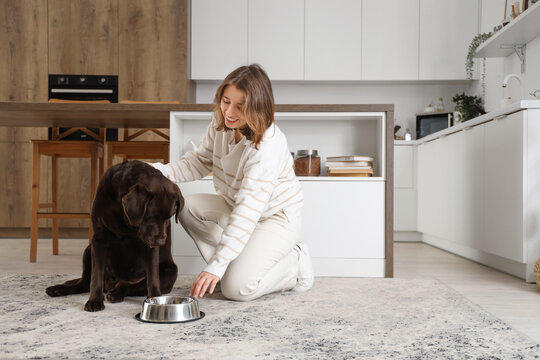 Young woman with Labrador dog and feeding bowl in kitchen