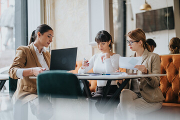 Three professional women are collaborating on a project. They are seated and engaged in discussion...