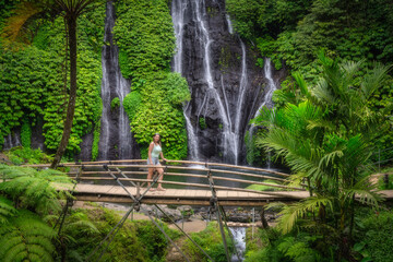 Obraz premium A woman on a bridge discovers and explore a breathtaking Banyumala Twin Waterfalls embraced by lush greenery, ideal destination for both nature enthusiasts and adventure seekers alike, Bali, Indonesia