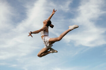 Blue sky with clouds, jumping. Young skinny fitness woman is outdoors