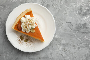 Piece of tasty homemade pumpkin pie with whipped cream, seeds and almond on grey table, top view. Space for text