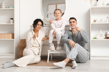 Fototapeta premium Happy family brushing teeth together in bathroom, promoting oral hygiene and healthy lifestyle for children and parents, the parents and their child are sitting on the floor and a small stool