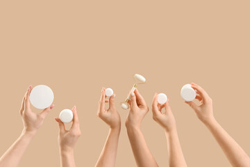 Many female hands with jars of cream and facial massage tool on beige background