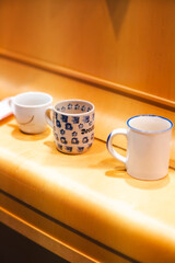 Three ceramic mugs of different designs and colors sit on a wooden surface in warm lighting. A cozy and nostalgic atmosphere, perfect for themes of home, coffee, tea, relaxation, and daily rituals.