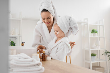 Cute little happy girl and her mother in bathrobes with cosmetic products applying cream at home